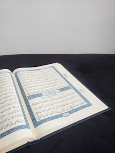 A serene scene of an open Qur’an beside a notebook with Arabic calligraphy, set on a soft off-white surface with gentle gold accents.