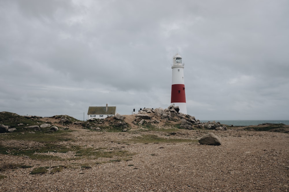 white and red lighthouse on brown sand near body of water during daytime