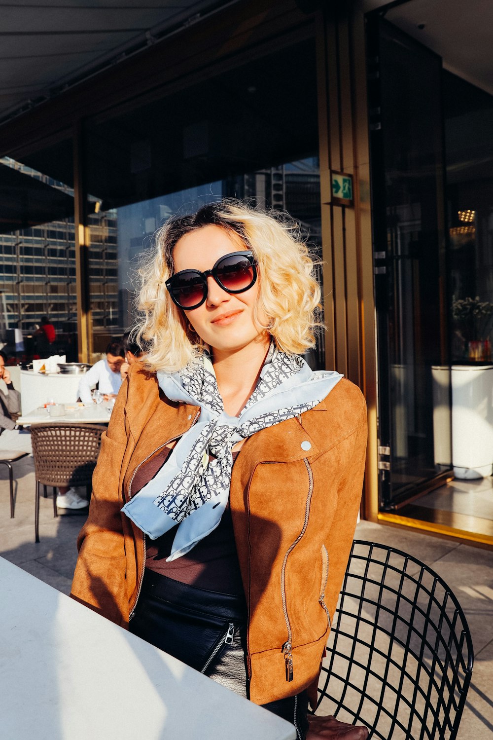 woman in brown coat wearing sunglasses sitting on brown chair