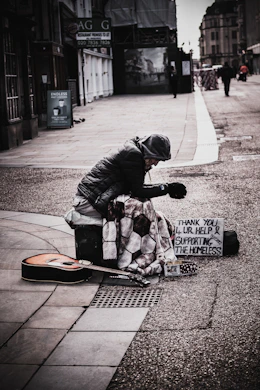A smiling homeless person receiving help, holding a card with a QR code, with a warm city background.