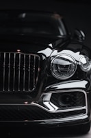 The front view of a luxury car, showcasing a prominent grille and sleek headlight design. The image highlights the glossy finish and intricate details of the vehicle, capturing its elegance and sophistication.
