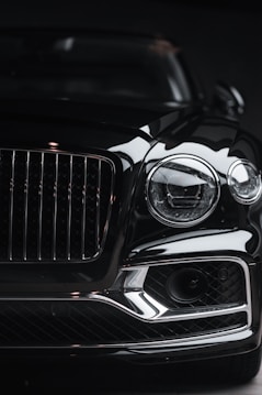 The front view of a luxury car, showcasing a prominent grille and sleek headlight design. The image highlights the glossy finish and intricate details of the vehicle, capturing its elegance and sophistication.