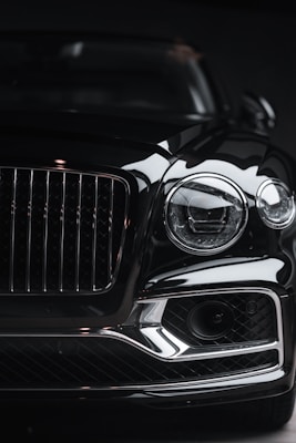 The front view of a luxury car, showcasing a prominent grille and sleek headlight design. The image highlights the glossy finish and intricate details of the vehicle, capturing its elegance and sophistication.