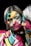 A person with a painted face and clothing features vibrant, abstract patterns in various colors. The person appears to be looking at their reflection in a mirror, with the painted patterns extending over the facial features creating an artistic and striking visual effect.