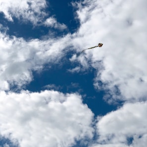 A vibrant kite soaring high against a bright blue sky with wispy clouds