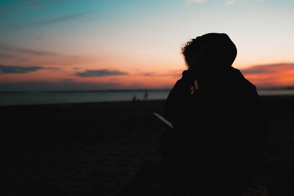 silhouette of woman sitting on beach during sunset