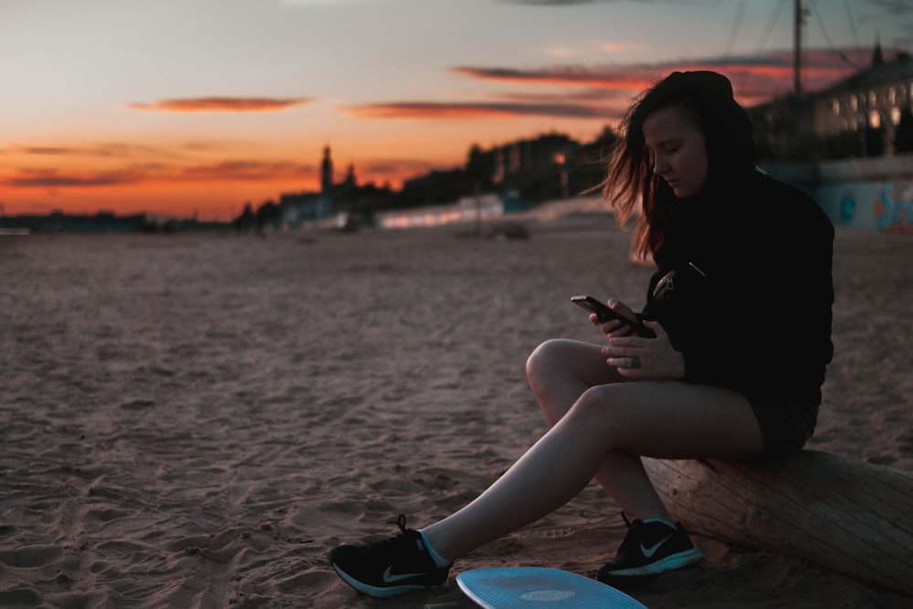 mulher na camisa preta e jeans jeans azuis sentados na praia durante o pôr do sol