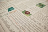 A close-up of a printed financial newspaper or report featuring numbers and text organized in columns and rows. There is a percentage symbol placed within a red circle on a green background, possibly indicating financial data or statistics.