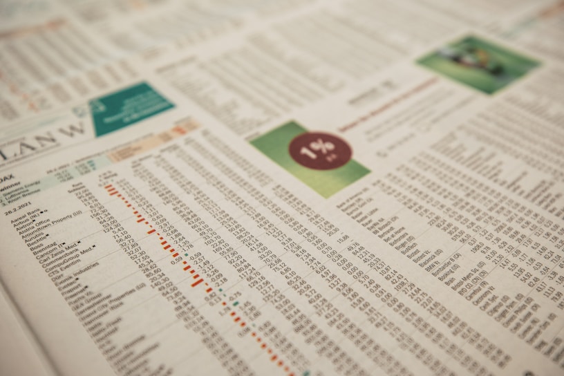 A close-up of a printed financial newspaper or report featuring numbers and text organized in columns and rows. There is a percentage symbol placed within a red circle on a green background, possibly indicating financial data or statistics.