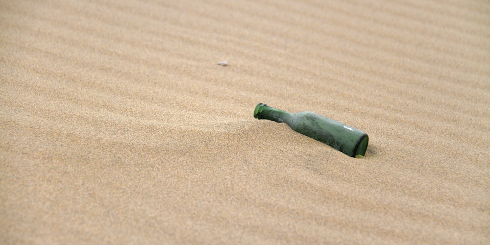 green and black glass bottle on brown sand