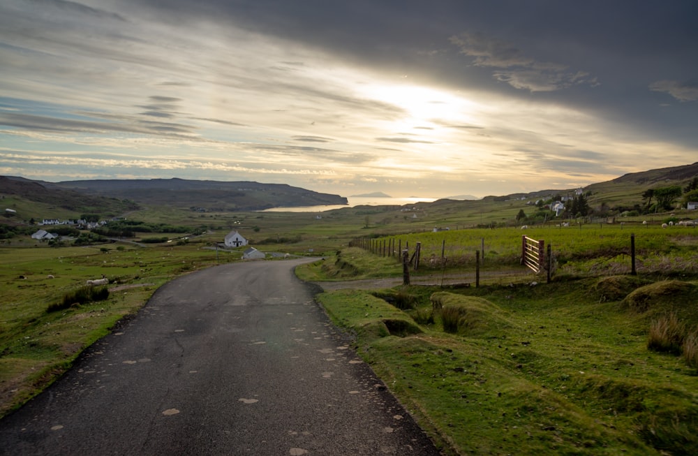 gray asphalt road between green grass field under cloudy sky during daytime