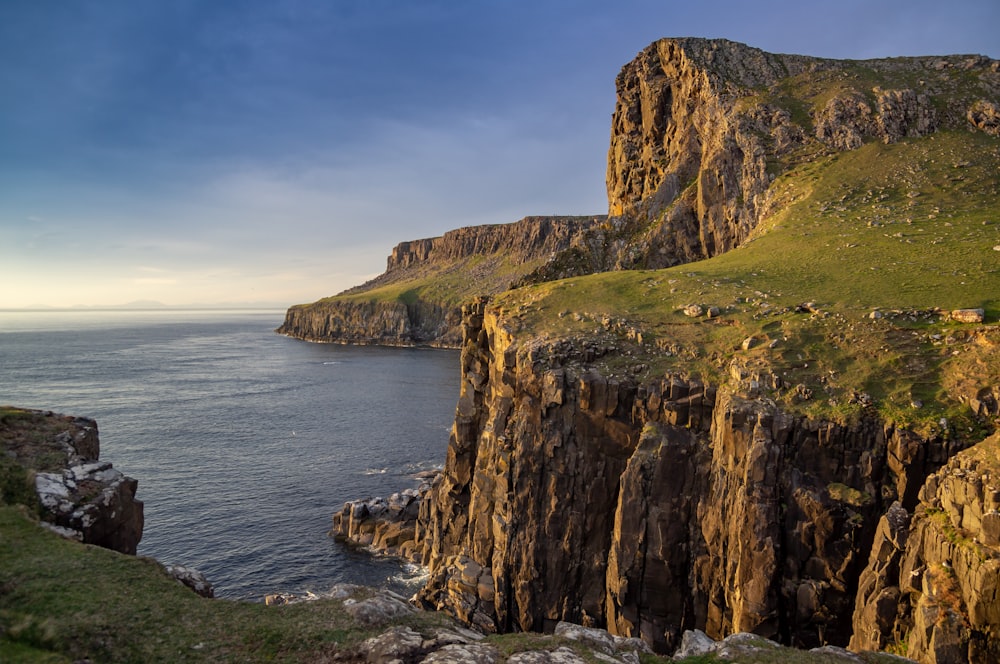 brown and green rock formation beside sea under blue sky during daytime