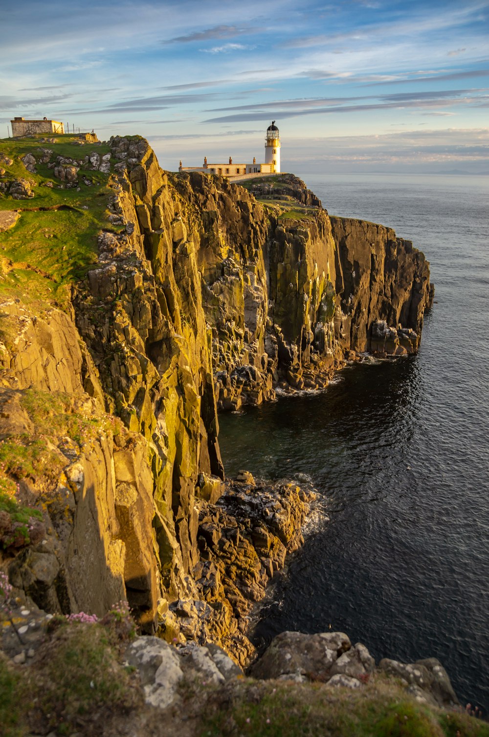 white and brown lighthouse on brown cliff beside body of water during daytime