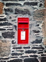 red mail box mounted on gray brick wall