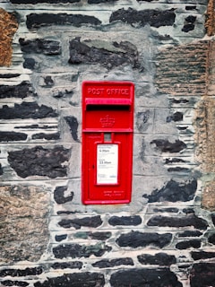 red mail box mounted on gray brick wall