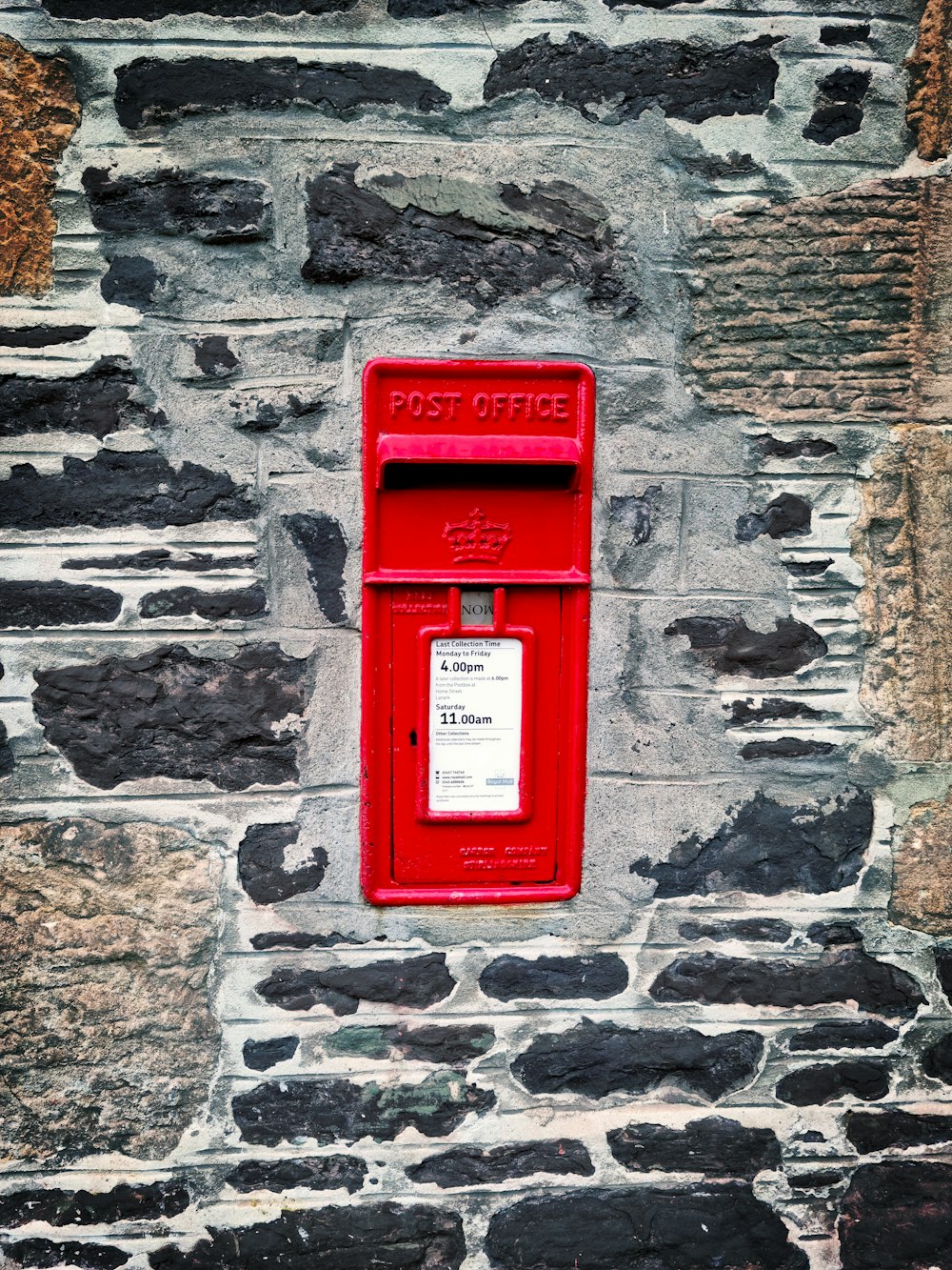 red mail box mounted on gray brick wall