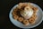 A cupcake with white cream frosting is topped and surrounded by several small round cookies. The cookies have a heart-shaped cutout in the center revealing some red filling. The arrangement is placed on a simple white plate against a dark background.