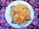 A large white plate filled with a generous serving of biryani rice, garnished with chunks of meat and potatoes. The dish is placed on a vibrant, patterned cloth featuring red and purple floral designs.