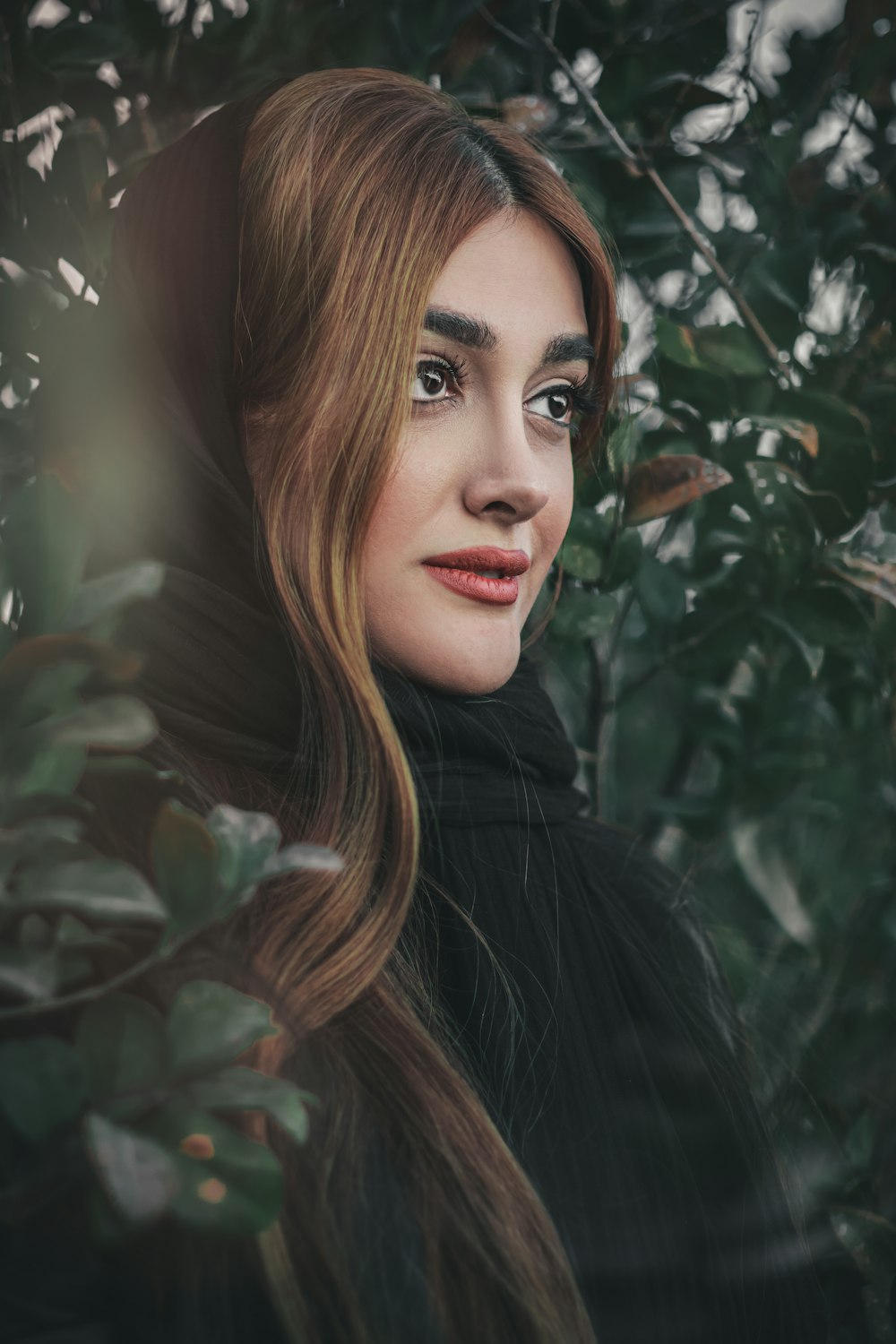 Frau im schwarzen Mantel neben grünen Blättern