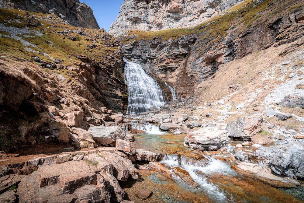 water falls between brown rocky mountains during daytime