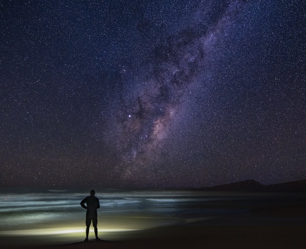 silhouette of man standing on seashore under starry night