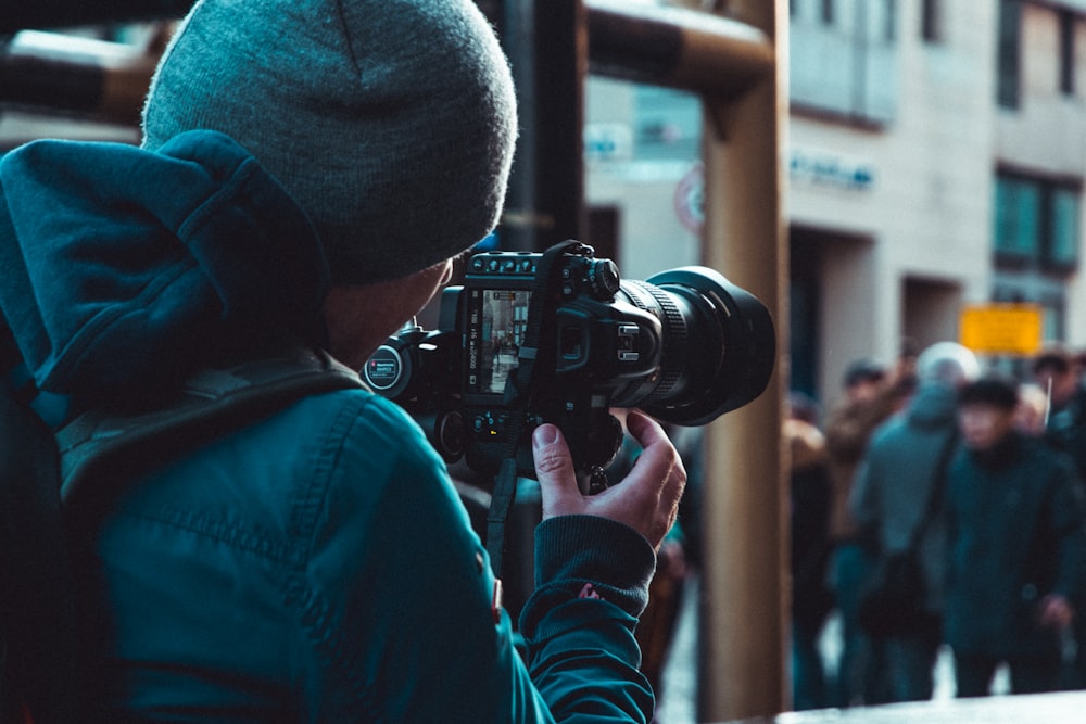 person in blue jacket holding black dslr camera