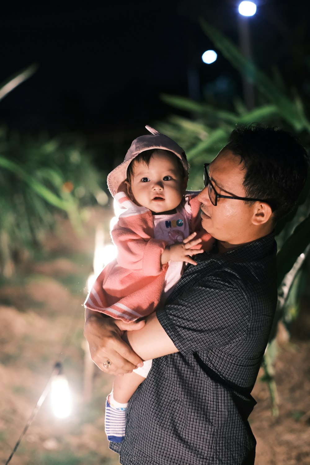 man in black and white pinstripe dress shirt carrying baby in pink hoodie