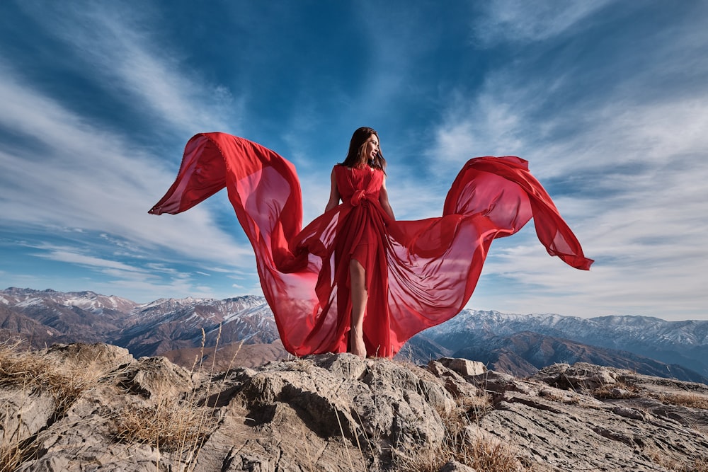 woman in red dress sitting on brown rock under blue sky during daytime