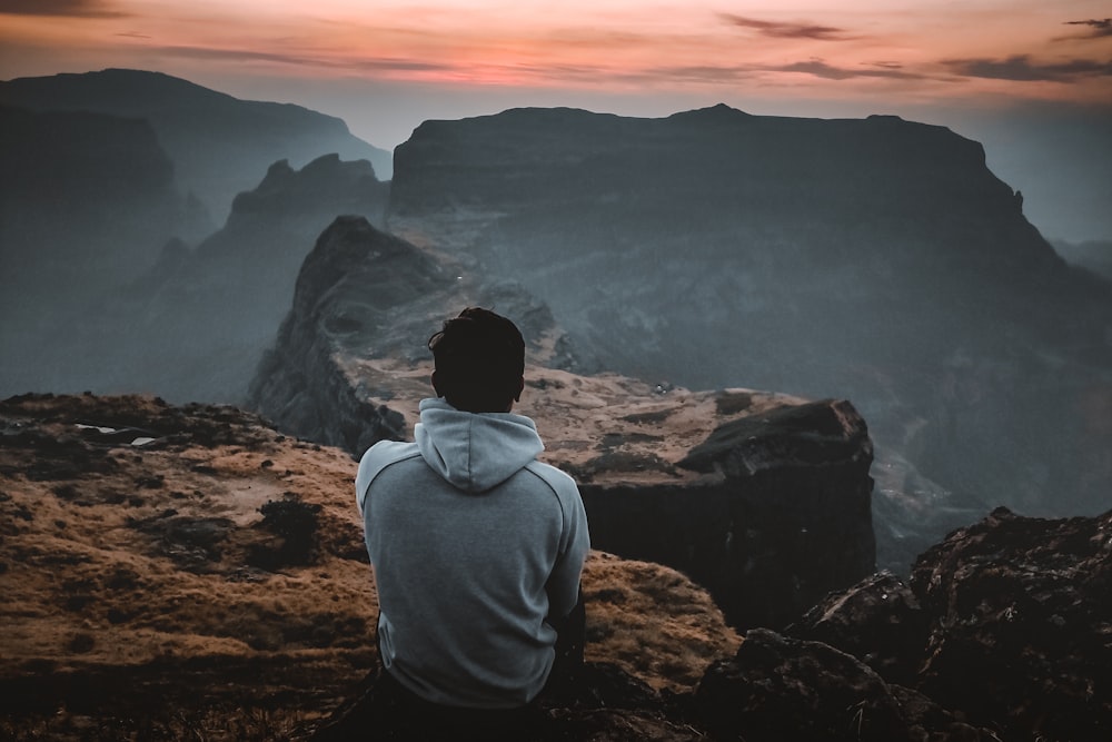 man in gray hoodie sitting on rock formation during daytime