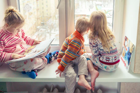 A warm nanny reading a storybook to two smiling children in a cozy living room.