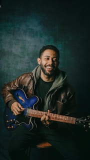 man in black leather jacket playing blue electric guitar