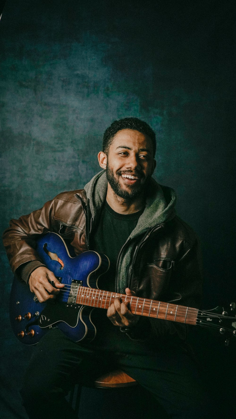 uomo in giacca di pelle nera che suona la chitarra elettrica blu