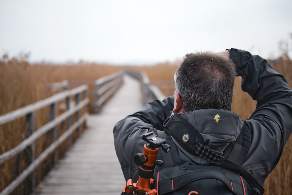 man in black jacket and black backpack sitting on wooden bridge during daytime