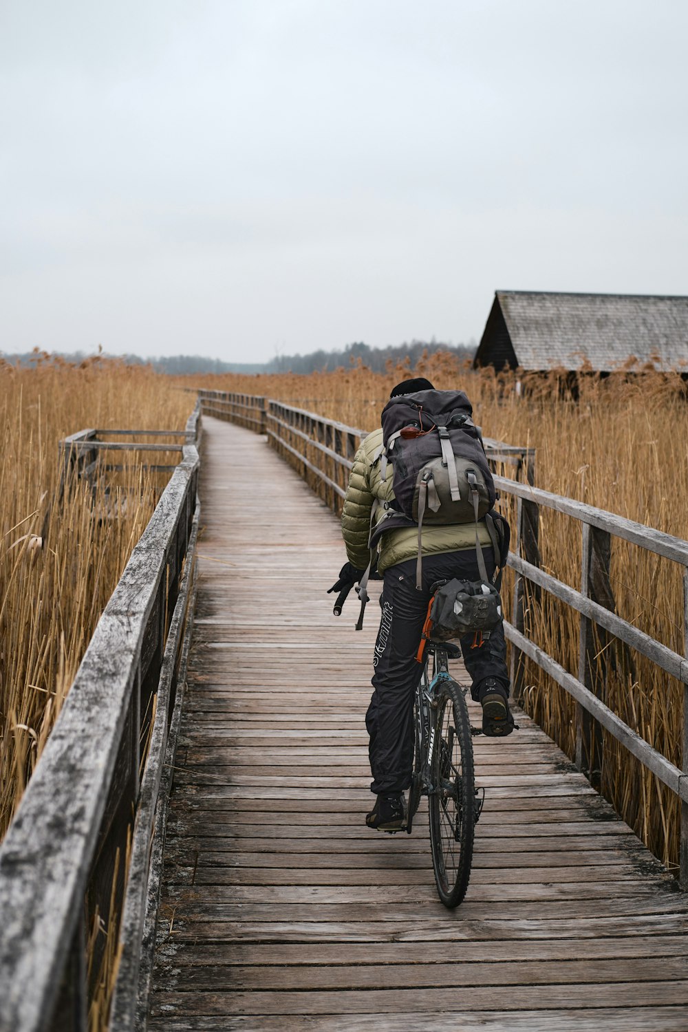 Hombre con chaqueta negra y mochila negra montando en bicicleta en puente de madera marrón durante el día