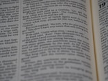 A close-up view of an opened book showing printed text in English. The focus is on the text in the central column, with surrounding text appearing slightly blurred due to the shallow depth of field.