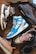A collection of stylish sneakers arranged on a wooden floor. The footwear features various designs, including high-tops and low-tops, with a mix of materials such as leather and fabric. The color palette includes bright blues, neutral earth tones, and bold blacks, with some sneakers showcasing unique branding details.