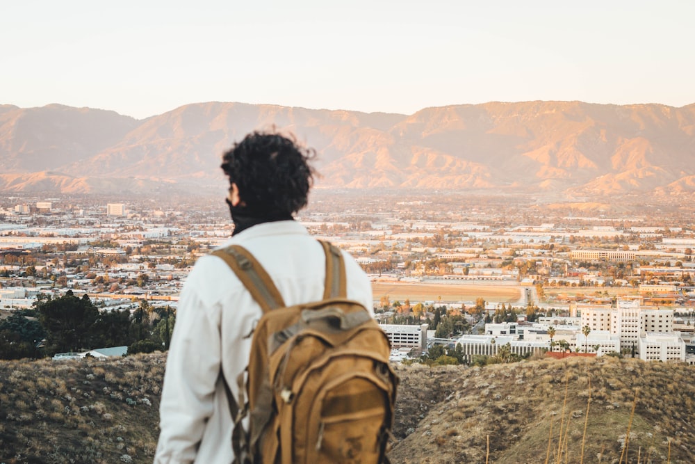 man in white shirt and brown backpack standing on top of mountain during daytime