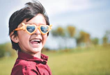 A cheerful toddler wearing colorful round glasses, smiling outdoors.
