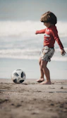 woman in red long sleeve shirt and white skirt holding soccer ball on beach during daytime