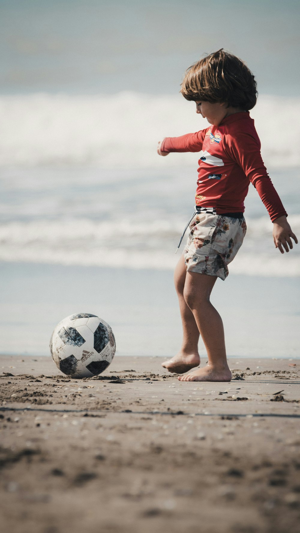 woman in red long sleeve shirt and white skirt holding soccer ball on beach during daytime