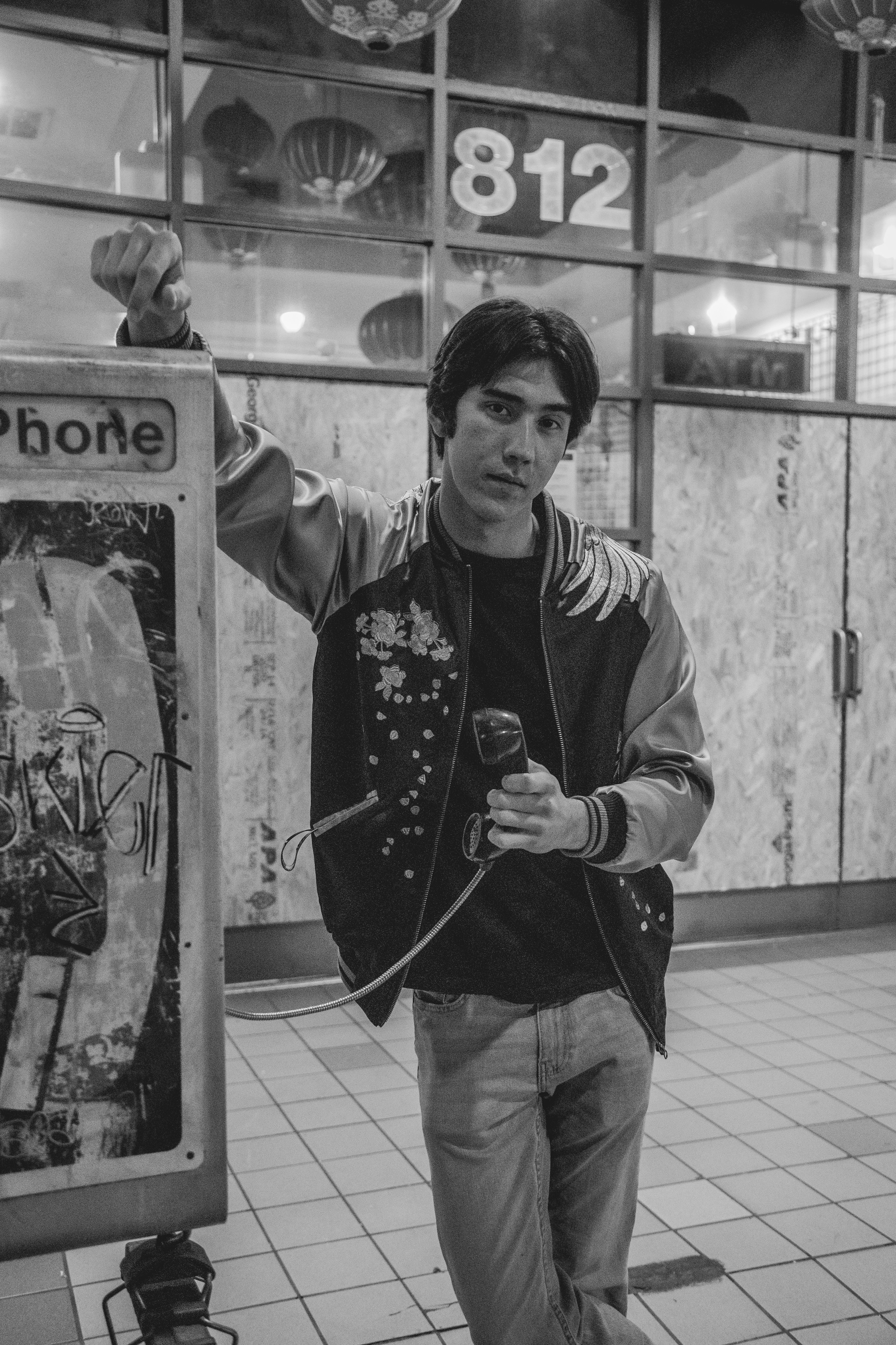 grayscale photo of man in zip up jacket holding telephone