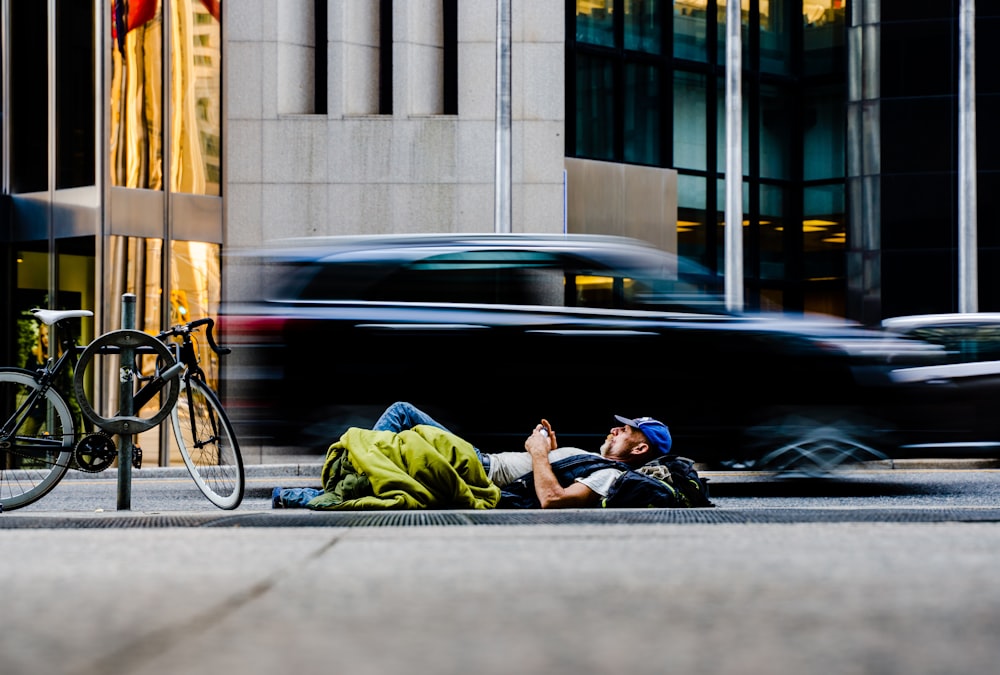 man in green jacket sitting on black road bike near black car during daytime