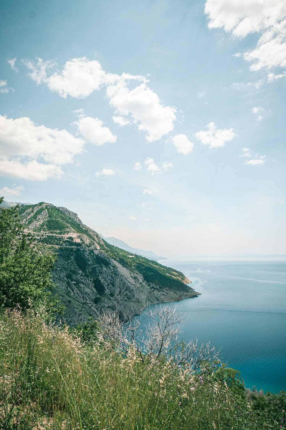 green mountain beside body of water under white clouds during daytime