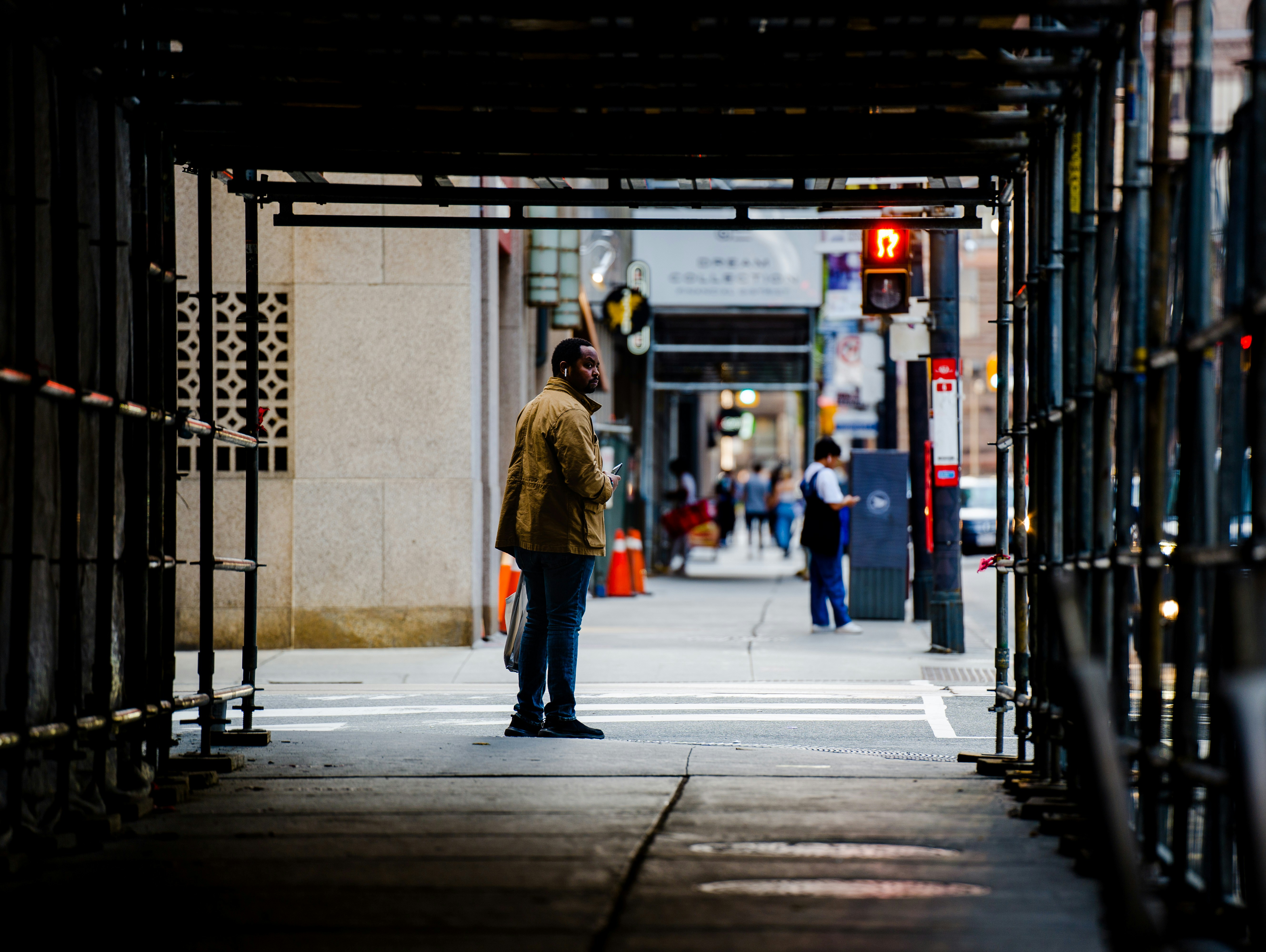 woman in brown coat standing on sidewalk during daytime