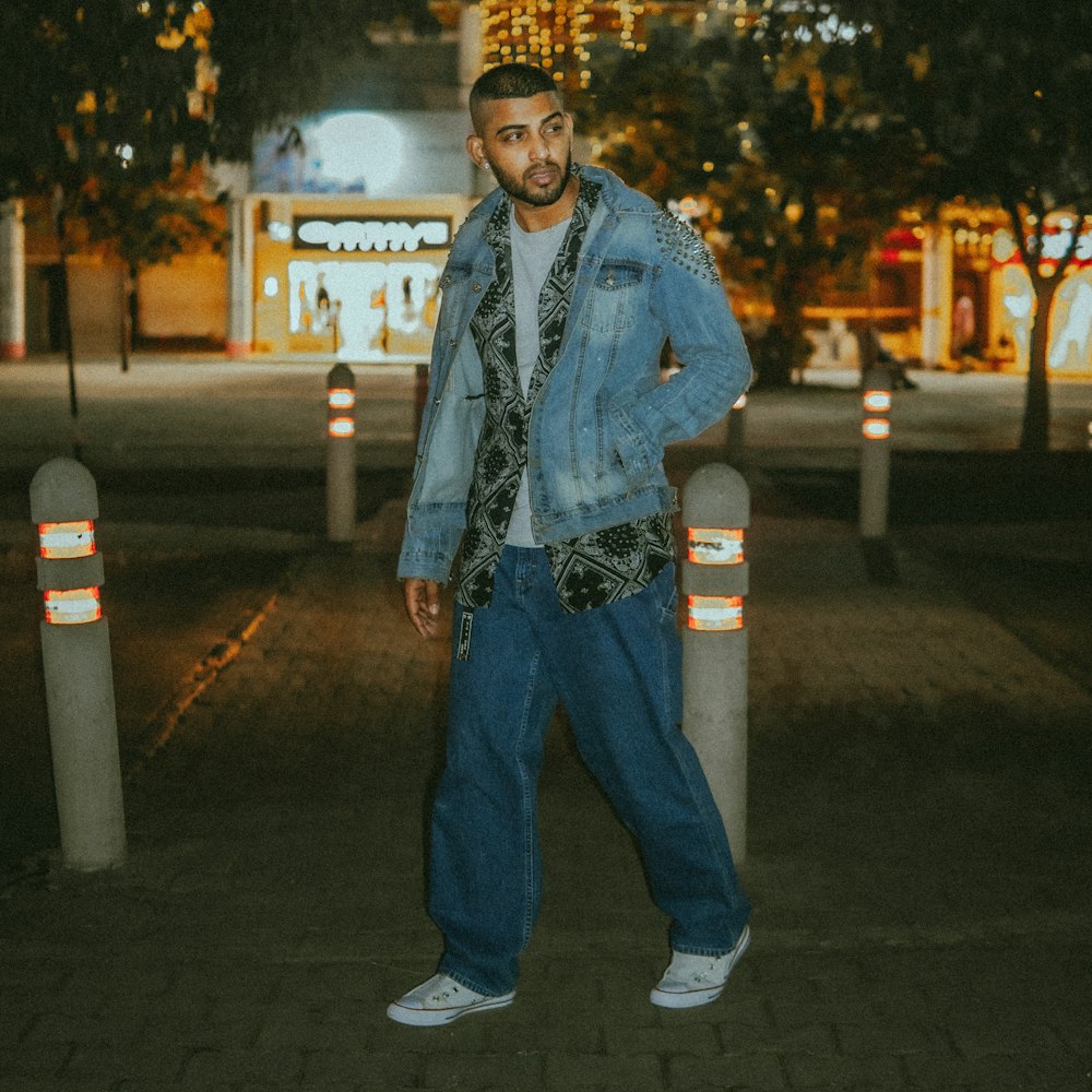 man in blue denim jacket standing on sidewalk during night time