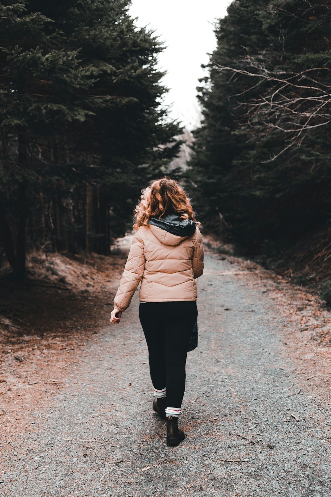 woman in beige jacket and black pants walking on road during daytime