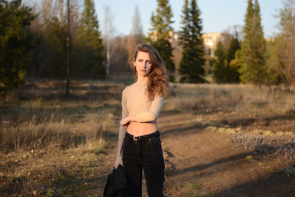 woman in white tank top and black pants standing on brown dirt road during daytime