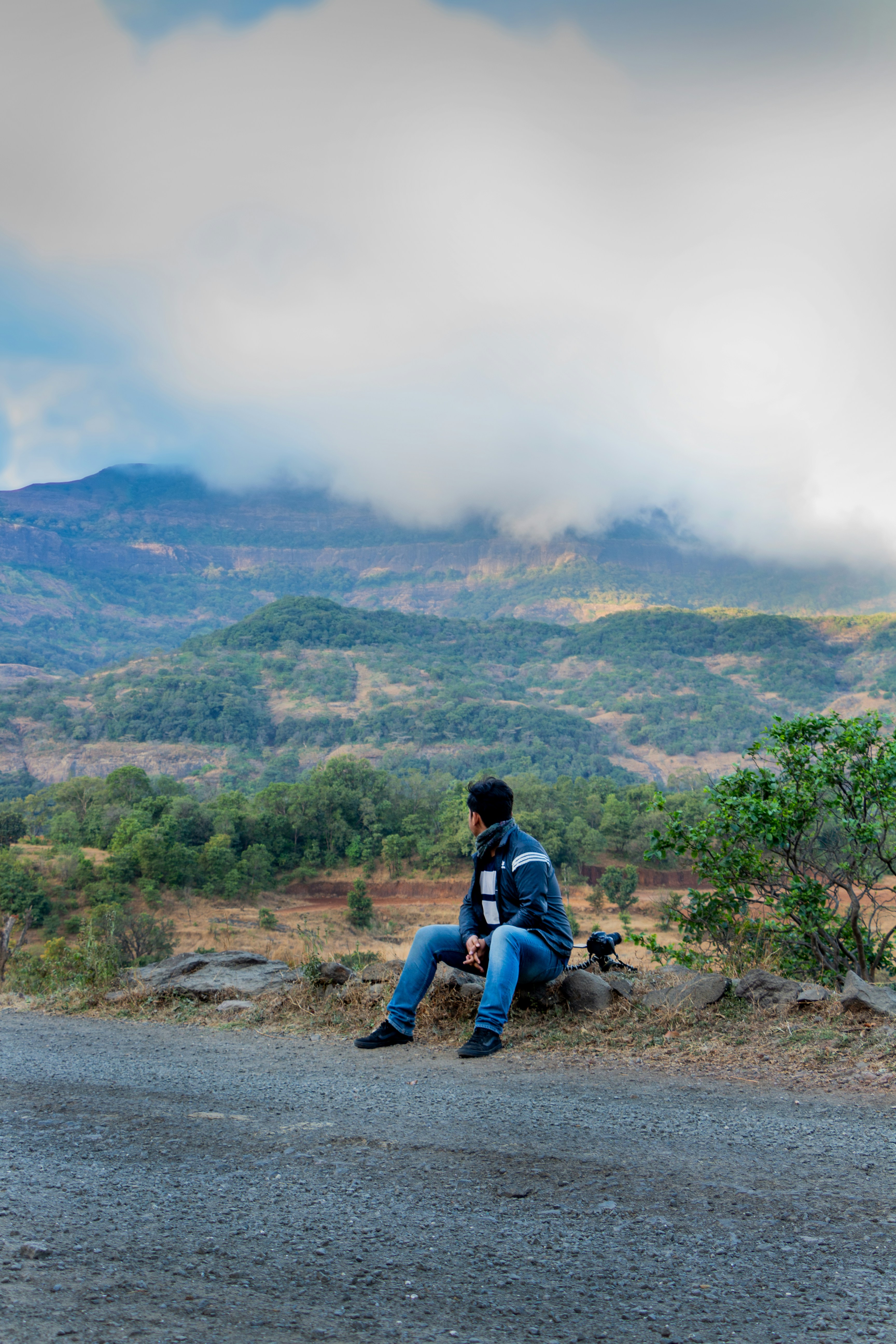 man in blue jacket sitting on gray rock near green grass field during daytime