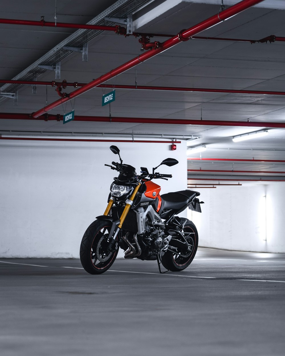 orange and black sports bike parked beside white wall