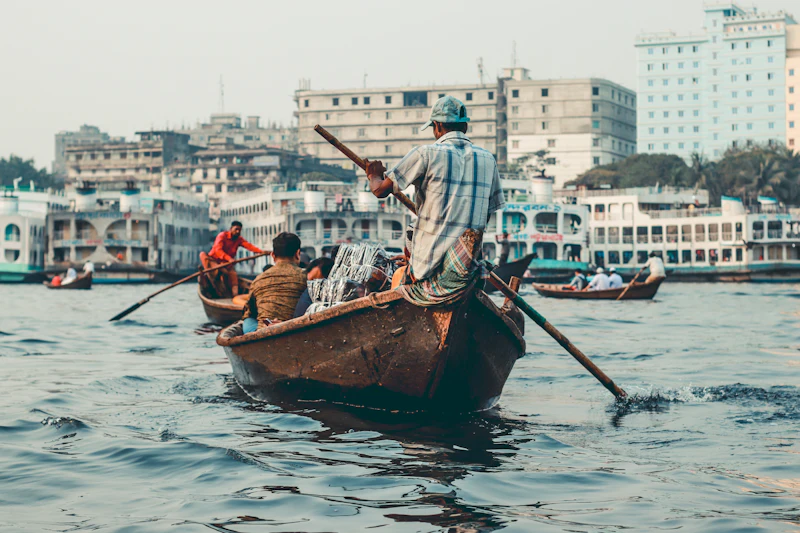 A boatman rowing across the Buriganga river in Dhaka, ferries moored behind
